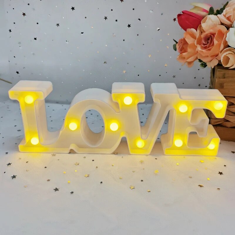 One white nightlamp that reads LOVE illuminated by yellow LED's on a white tablecloth with silver and red heart glitter