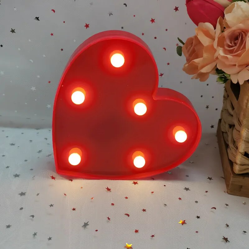 One red nightlamp heart illuminated by yellow LED's on a white tablecloth with silver and red heart glitter