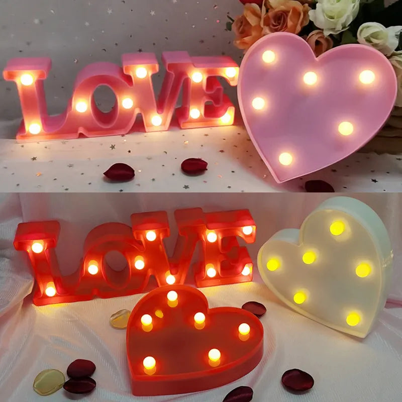 Two red nightlamps that read LOVE and a white and pink heart lamp all illuminated by yellow LED's on a white tablecloth with silver glitter