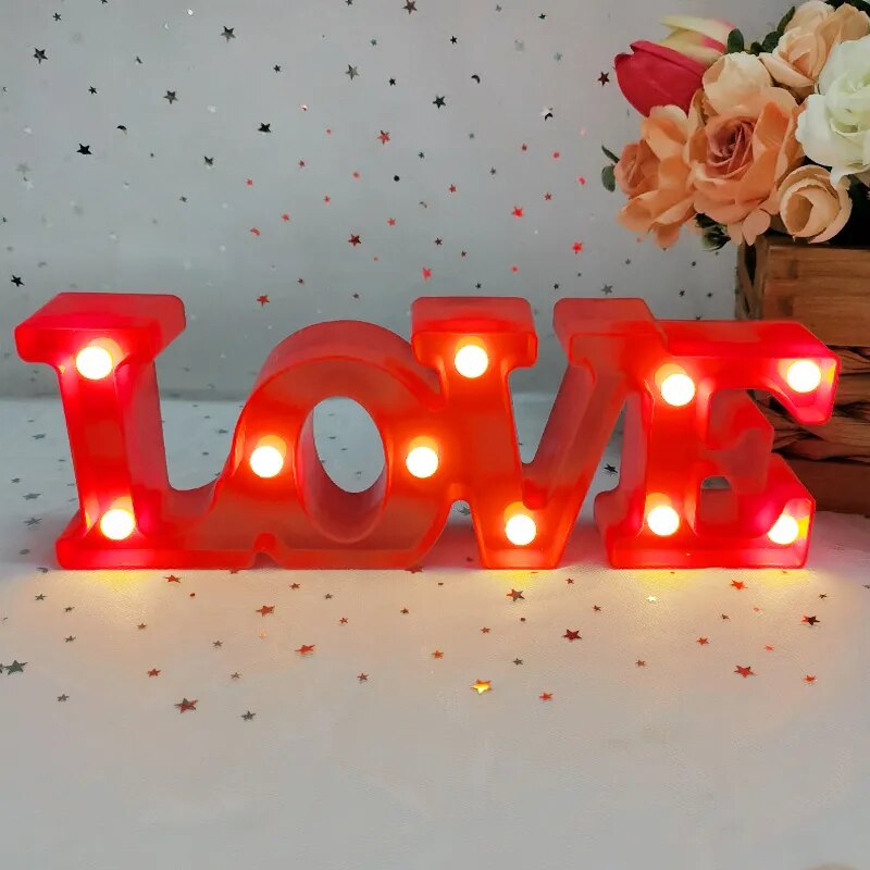 One red nightlamp that reads LOVE illuminated by yellow LED's on a white tablecloth with silver and red heart glitter