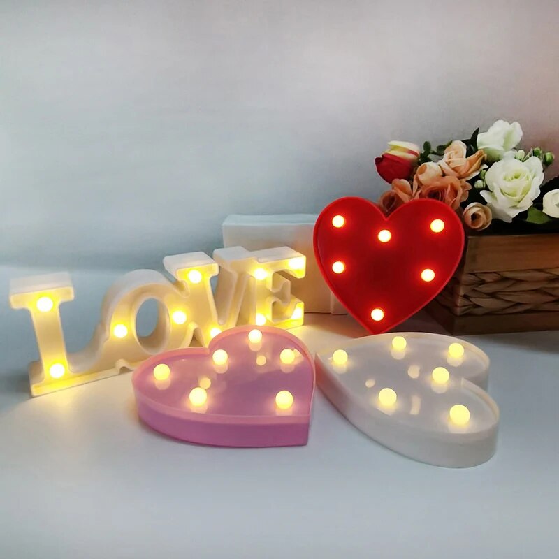 One white nightlamp that reads LOVE and a red, white, and pink heart lamp all illuminated by yellow LED's on a white tablecloth with silver glitter