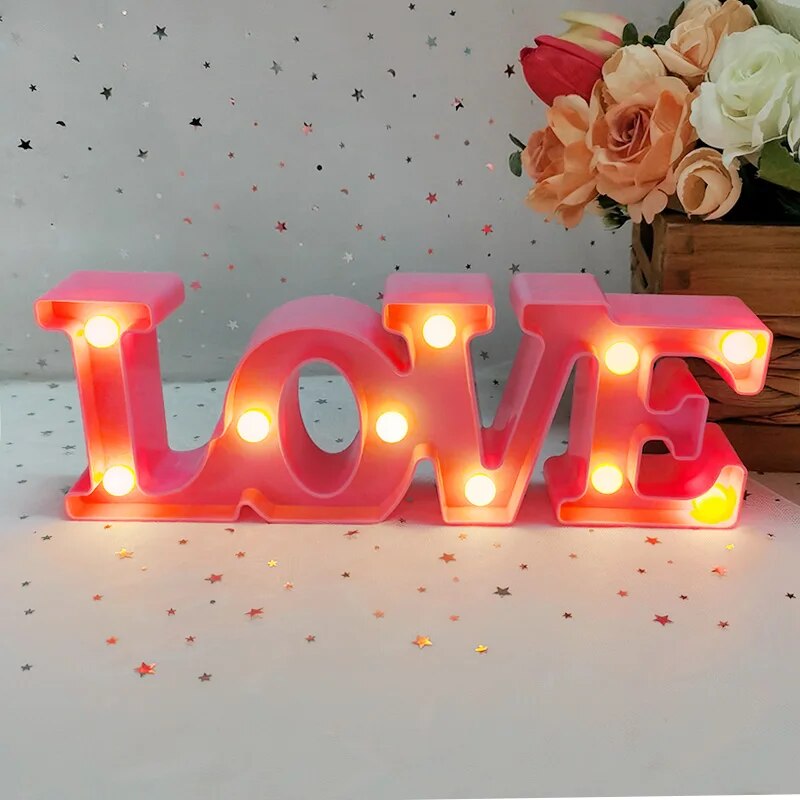 One red nightlamp that reads LOVE illuminated by yellow LED's on a white tablecloth with silver and red heart glitter