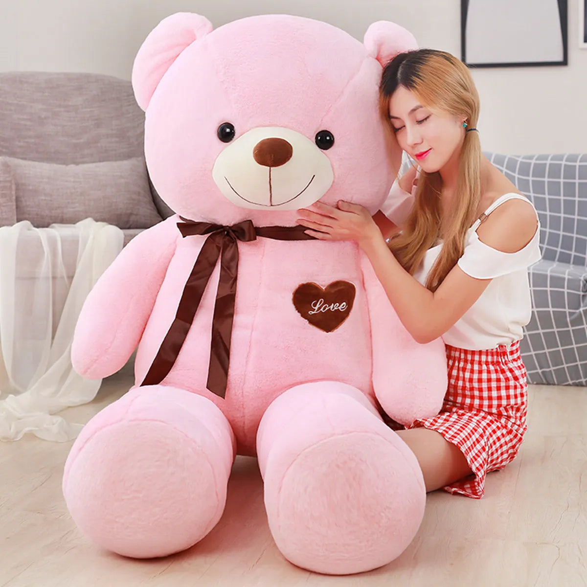 Large pink teddy bear wearing dark brown scarf and dark brown heart that reads love in pink lettering