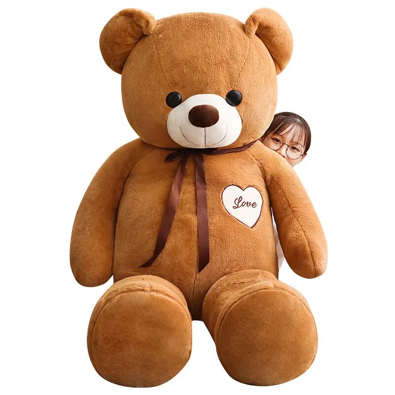 Large brown teddy bear wearing brown scarf and white heart that reads love in brown lettering