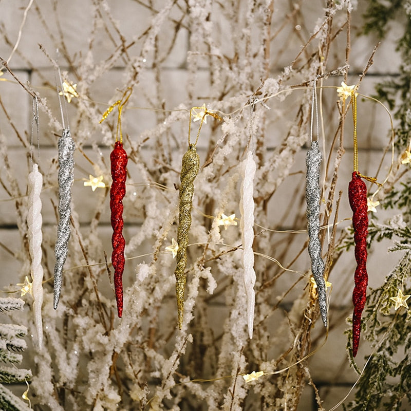 Two white, red and grey and one gold icicle Christmas tree ornaments suspended in snow covered deciduous bush