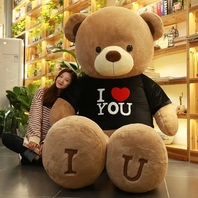 Brown teddy bear wearing a black t-shirt reading I Love You and I and U written in brown lettering on feet