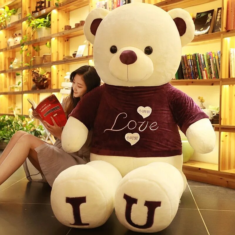 Large light beige teddy bear wearing brown t-shirt with I and U written on feet in brown lettering