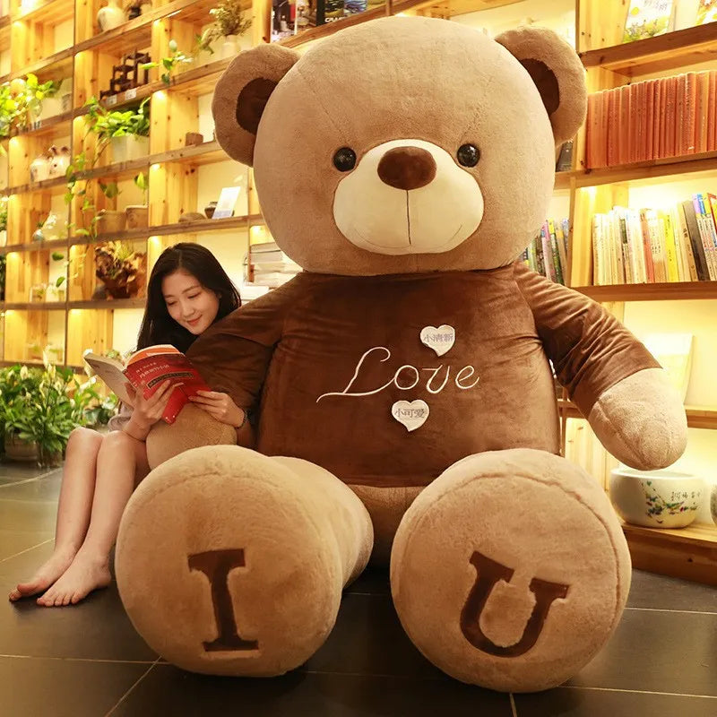 Large light brown teddy bear wearing brown t-shirt with I and U written on feet in dark brown lettering