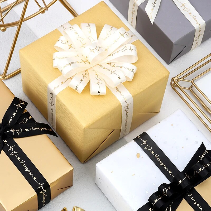 Gold colored present with white ribbon that reads I love you on a white table