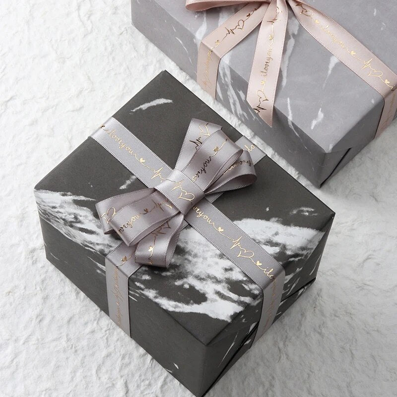 Two grey presents with grey ribbon that reads I love you on a grey table