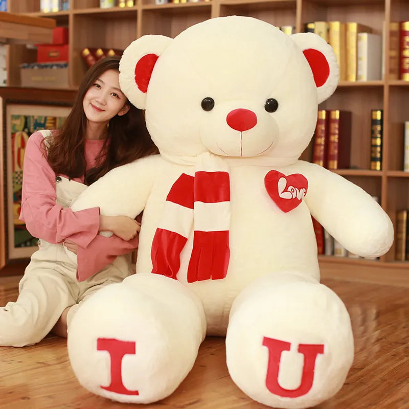 Large white teddy bear wearing red and white scarf with I and U written on feet in red lettering