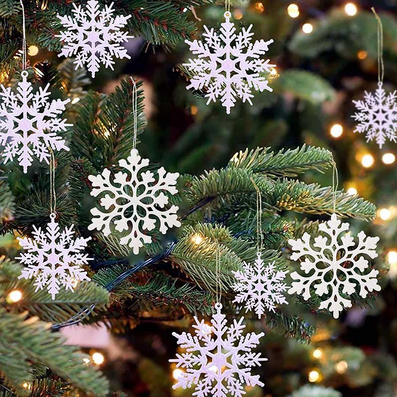 Close up of eight white snowflake Christmas tree ornamnts on green artificial Christmas tree with yellow LED lights