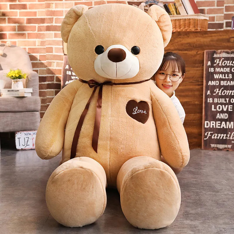 Large beige teddy bear wearing brown scarf and brown heart that reads love in white lettering