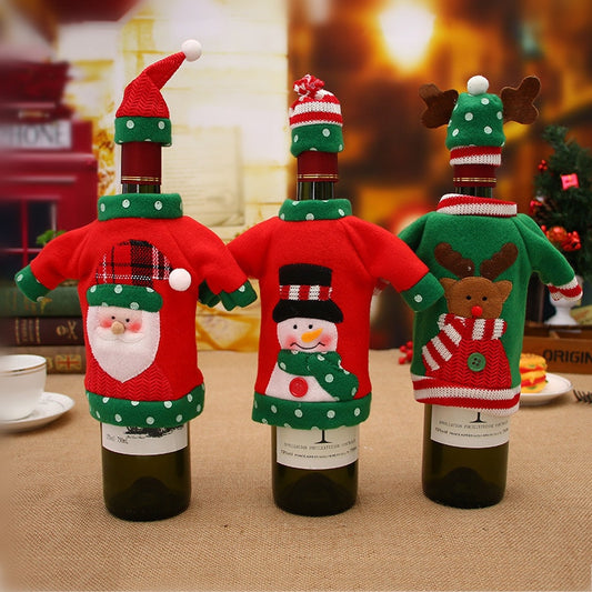 Three wine bottles with Christmas covers. First has a red sweater with a snowman, second has a green sweater with a reindeer and third has a red sweater with a snowman on a table